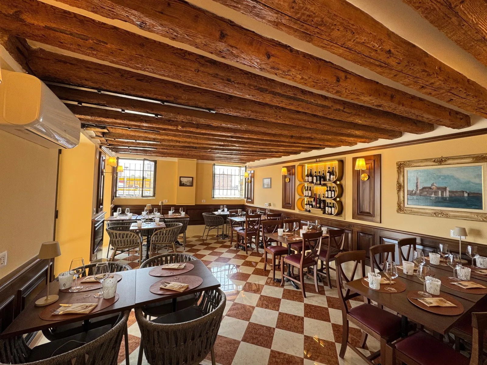 The dining room of Trattoria San Basilio with exposed wooden beams and a burgundy chequered floor